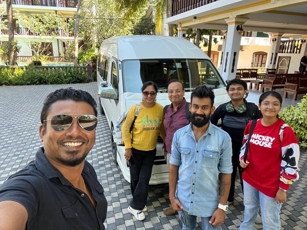 Ceylon Now driver-guide with a family beside the white high-roof tourist van under a hotel portico in Sri Lanka