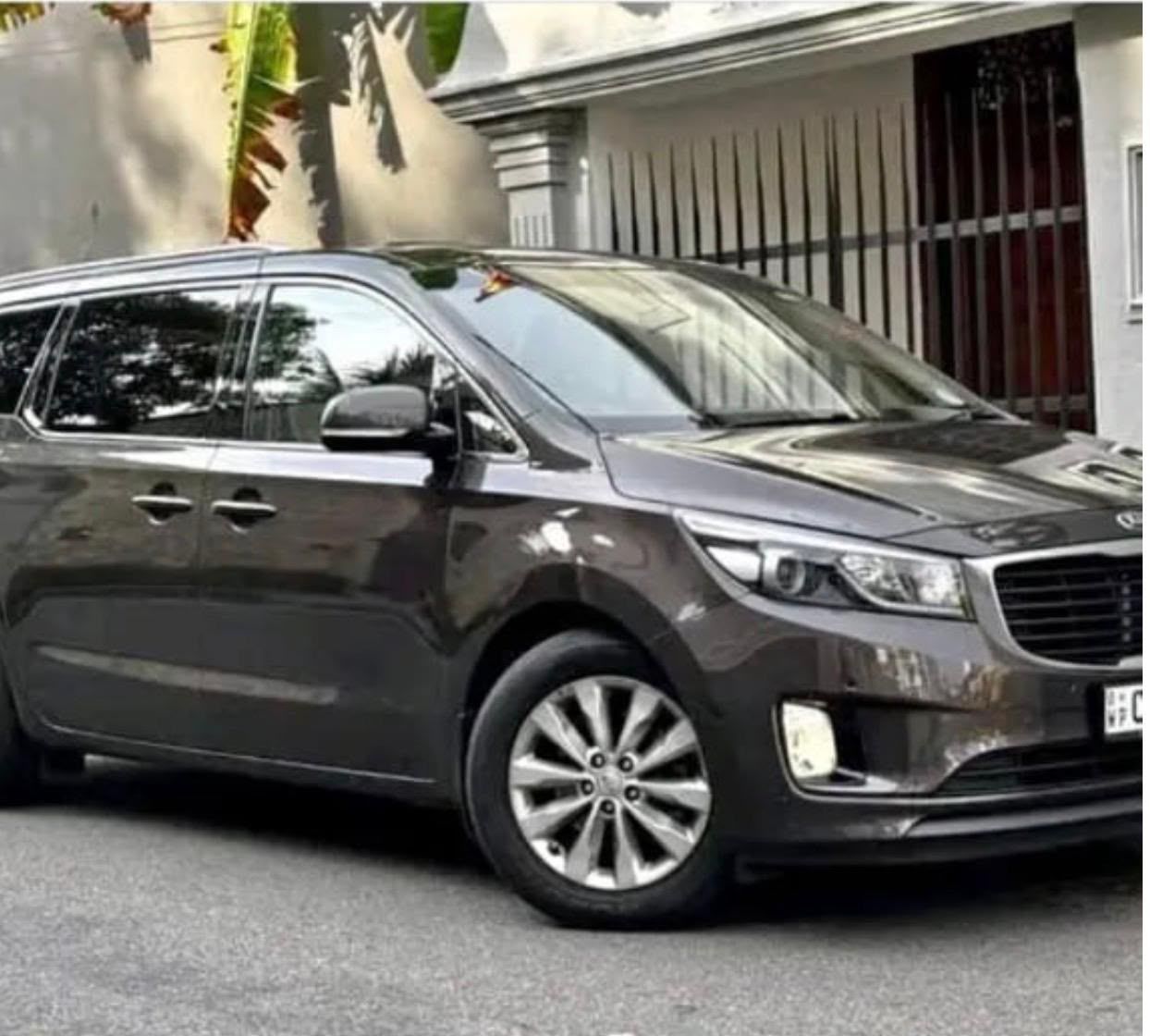 Ceylon Now Family MPV, a dark grey 7-seat Kia Carnival, parked outside a house in Sri Lanka